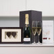 Engagement Champagne Gift Set: A bottle of champagne with two fluted glasses is displayed alongside a framed picture of two hearts and a brochure for Galway Prosecco. The items are arranged on a white countertop against a light background. Engagement Champagne Gift Set: A bottle of champagne with two fluted glasses is displayed alongside a framed picture of two hearts and a brochure for Galway Prosecco. The items are arranged on a white countertop against a light background.